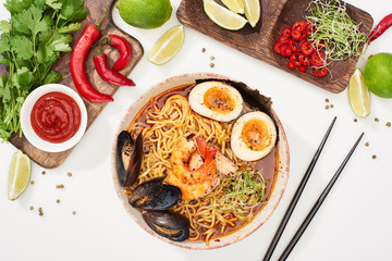 top view of spicy seafood ramen near fresh ingredients and chopsticks on white surface