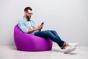Full length profile photo of positive guy sitting comfy violet armchair holding telephone chatting...