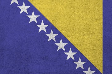 Bosnia and Herzegovina flag depicted in bright paint colors on old relief plastering wall. Textured...