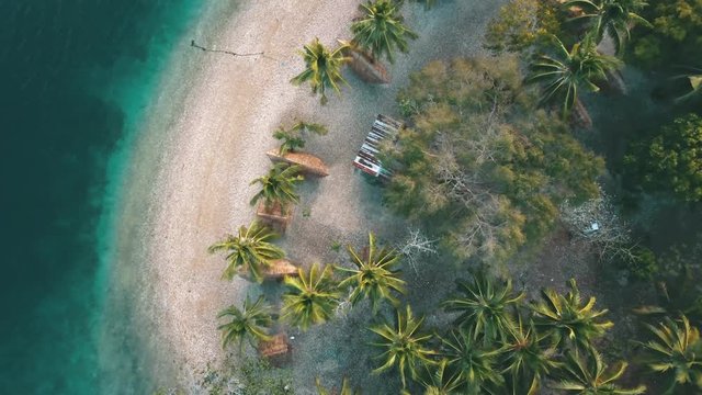a downward shot flying up oaf a beach with some bungalows and a palm trees