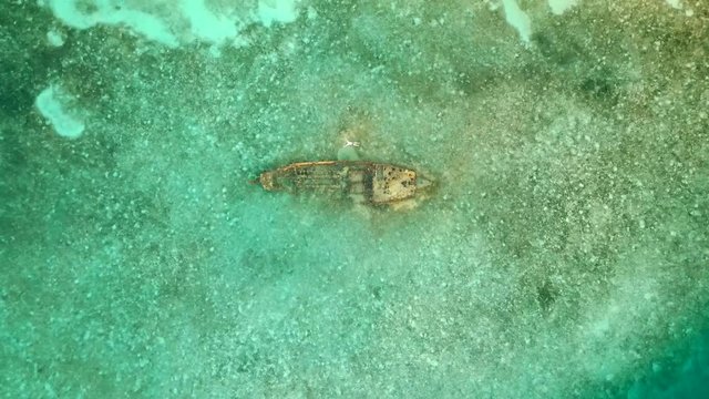 flying over a sunken ship rocks with people snorkelling around it.