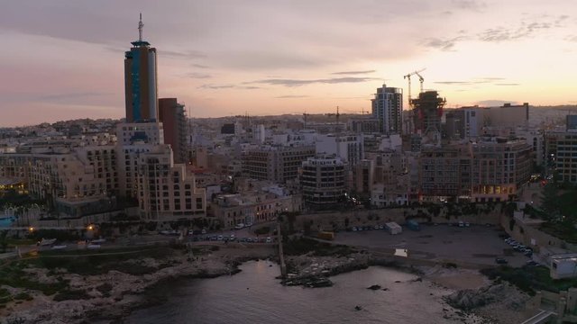 High Aerial shot orbiting around the coast of St Julians Malta. Baech and bay at the sunset