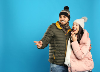 Happy young couple in warm clothes on blue background, space for text. Winter vacation