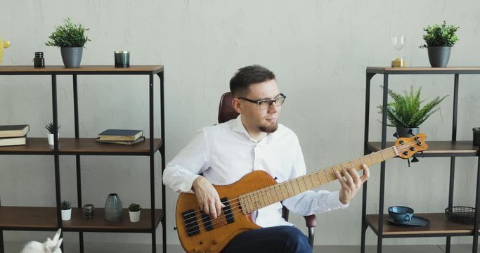 Guy practicing musical instrument. amera is moving to man. Office worker is playing on guitar and enjoying it sitting at work during break. Busnessman busy with his music hobby in workplace.