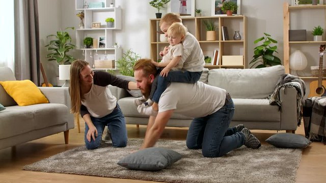 young dad crawling on floor carrying cute small child sons on back