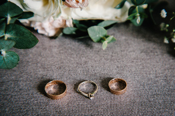 Wedding accessories: flowers, buttonhole, gold wedding rings on rustic sacking, retro brown background. holiday concept. Stylish bouquet of flowers of the bride. Close up.