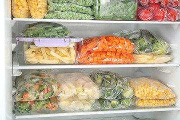 Plastic bags and containers with different frozen vegetables in refrigerator