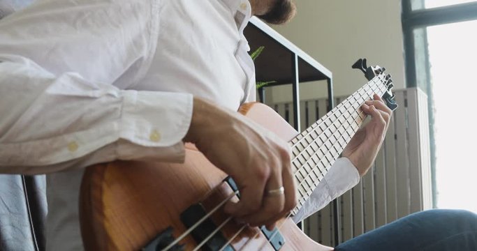 Man busy with music hobby in workplace. Businessman is playing on guitar and enjoying it sitting in office, side view. Guy practicing musical instrument. amera moves away from man's hands on guitar.