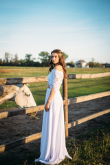 Fototapeta premium boho wedding. Beautiful and stylish girl bride on a nature horse farm. One on the green field background. White lace dress, hair accessories.