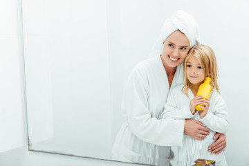 cheerful mother hugging daughter with bottle of shampoo