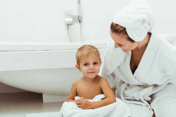 happy mother smiling while looking at toddler boy in bathroom