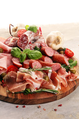 Food tray with delicious salami, pieces of sliced prosciutto crudo, sausage and basil. Meat platter