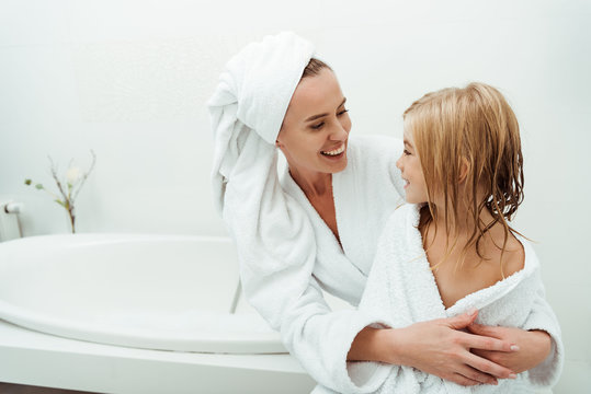 happy mother smiling while looking at daughter in bathroom