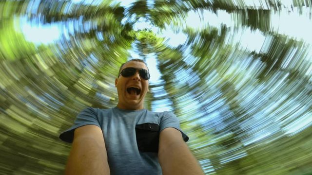 Funny happy caucasian Tourist guy rotates and spins in forest, smiles and screams. Bottom view and low angle shot of tree crowns. Green nature for background. Durmitor national park, mountain massif