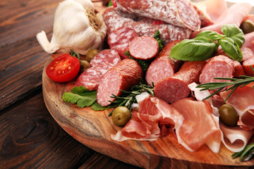 Food tray with delicious salami, pieces of sliced prosciutto crudo, sausage and basil. Meat platter