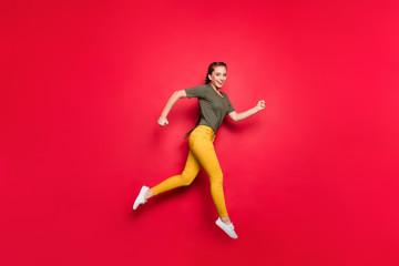 Full length profile photo of active lady jumping high competition marathon participant running fast wear casual yellow pants green t-shirt isolated red color background