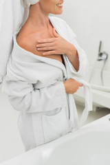 cropped view of cheerful woman in bathrobe touching body in bathroom