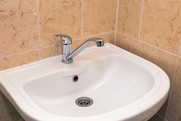 Chrome faucet on white ceramic wash basin in the bathroom.