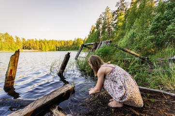 Woman sitting on the shore by the lake washes her hands