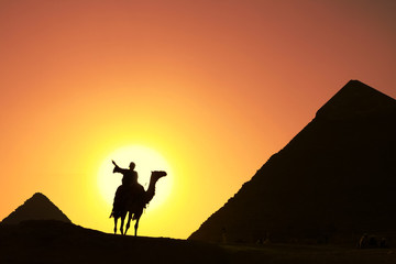 Fototapeta na wymiar camel bedouin silhouette at giza pyramids cairo egypt at sunset