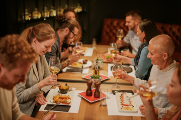 Group of best friends having dinner at restaurant. They all holding glasses of white  wine, smiling and talking.