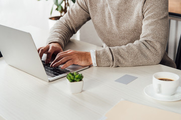 Cropped view of man typing on laptop keyboard beside card with copy space on table