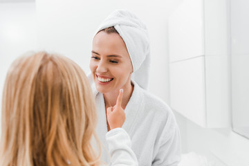 back view of kid applying cosmetic cream face of happy mother