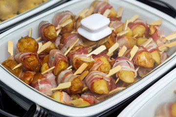Roasted potatoes with bacon in marmite, potatoes wrapped in bacon and fastened with a wooden skewer.