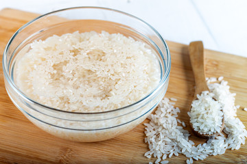 Soaked rice, grain, cloudy liquid water in glass bowl on wooden background