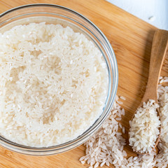 Soaked rice, grain, cloudy liquid water in glass bowl on wooden background