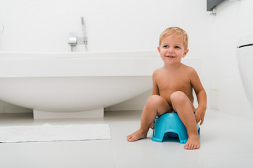 happy toddler boy sitting on blue potty near bathtub