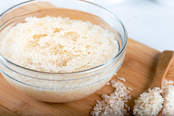 Soaked rice, grain, cloudy liquid water in glass bowl on wooden background