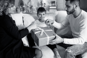 Young parents unwrapping presents with their little son.