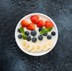 Delicious, healthy and balanced Breakfast of oatmeal with berries and fruit in a plate on the left on a concrete background. Horizontal orientation. Top view