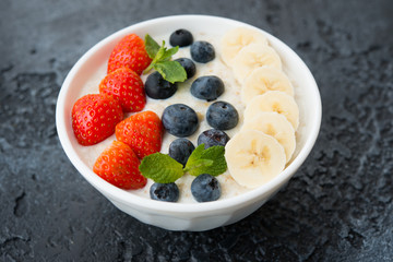 Delicious, healthy and balanced Breakfast of oatmeal with berries and fruit in a plate on the left on a concrete background. Horizontal orientation. Close up