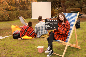 Happy young woman with movie clapper in outdoor cinema