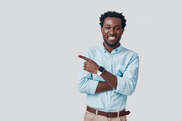 Handsome young African man pointing copy space and smiling while standing against grey background