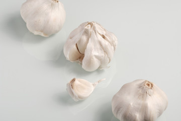 Closeup of three white and dry garlic bulbs and a clove of garlic lying on a white glass plate