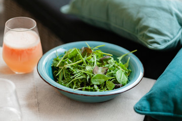 Healthy and light calories free lunch in vegan restaurant - fresh green salad and freshly squeezed orange juice with pulp. Raw seasonal ingredients. Close up, front view.
