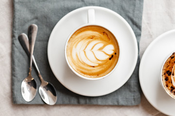 Every day morning routine: two cups of delicious creamy cappuccino, romantic breakfast for couple. Soft day light, close up, natural cotton background. Top view flat lay