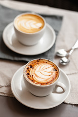 Every day morning routine: two cups of delicious creamy cappuccino, romantic breakfast for couple. Sift day light, close up, natural cotton background
