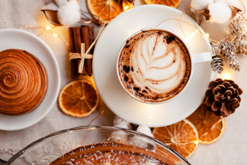 Cozy and romantic holiday time. Winter hot drink in white cup. Christmas lights on, festive mood, atmosphere of relax, family time. Flat lay, top view, white background.
