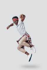 Full length of playful young African man smiling while hovering against grey background