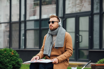 Blind man in headphones reading book on bench in park