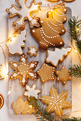 Delicious homemade gingerbread cookies with white icing. Christmas lights, branch of fir tree, dry orange slices. White wooden background, flat lay, top view. Festive holiday atmosphere, family time