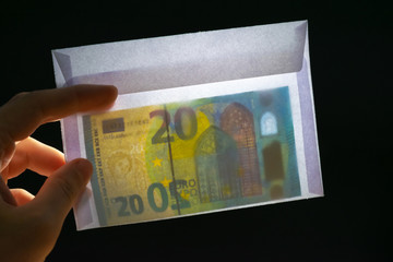 Envelope with twenty euros bill in it. Deep black background. Hand holds the envelope.