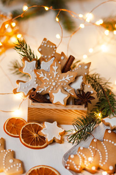 Wooden box with delicious homemade gingerbread cookies decorated with icing. Rustic decor, christmas lights on. Festive mood, holiday atmosphere. Front view, closeup, white background