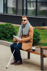 Obraz premium Blind man holding headphones while sitting on bench