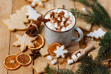 Obraz na płótnie Canvas Winter hot drink: white mug with hot chocolate with marshmallow and cinnamon. Cozy home atmosphere, festive holiday mood. Rustic style, wooden background. Homemade gingerbread cookies, white icing