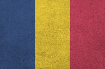 Chad flag depicted in bright paint colors on old relief plastering wall. Textured banner on rough...